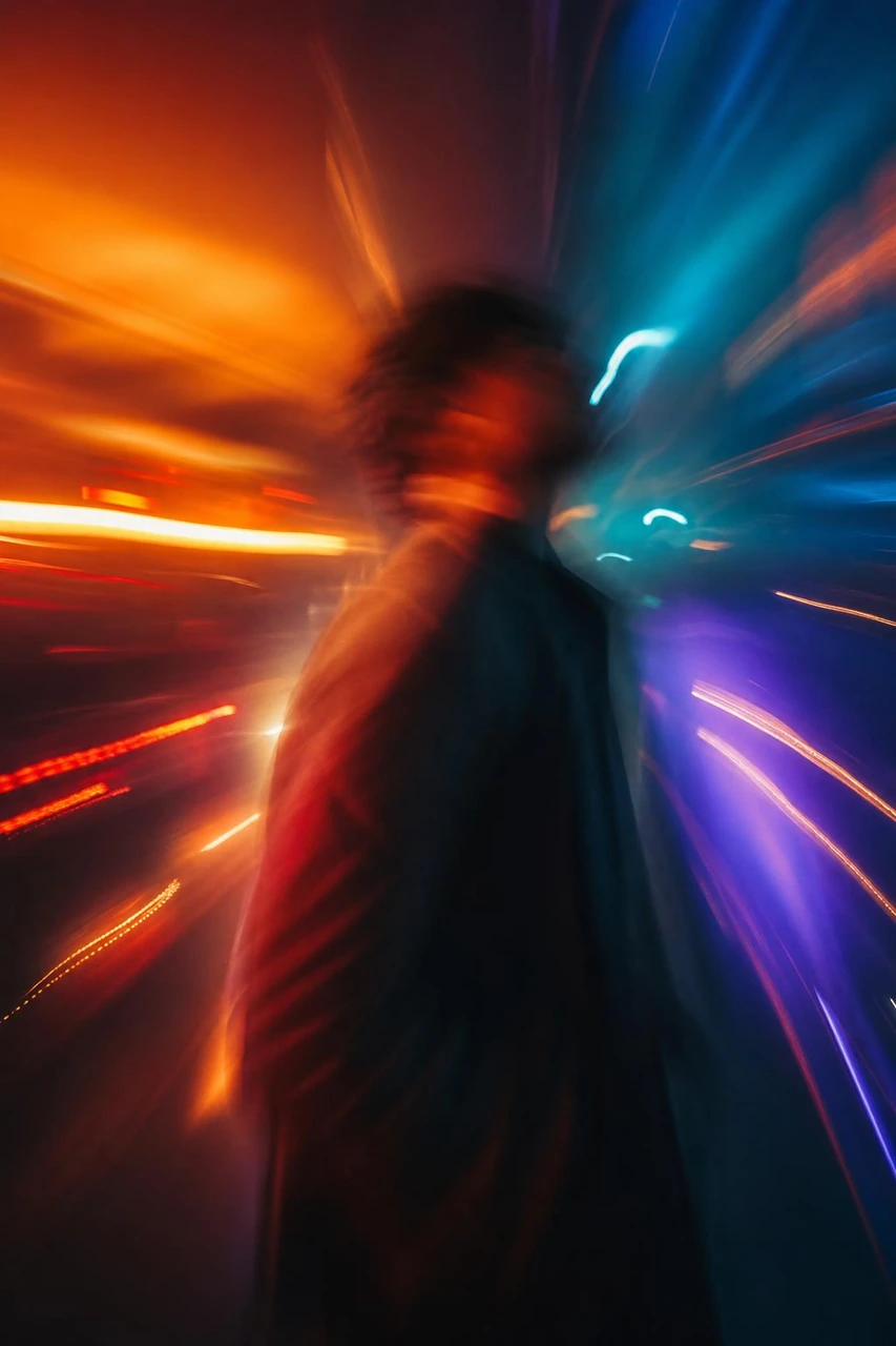 Create a cinematic abstract portrait of a blurred figure surrounded by dynamic neon light streaks, blending warm orange tones with cool blue and purple highlights.