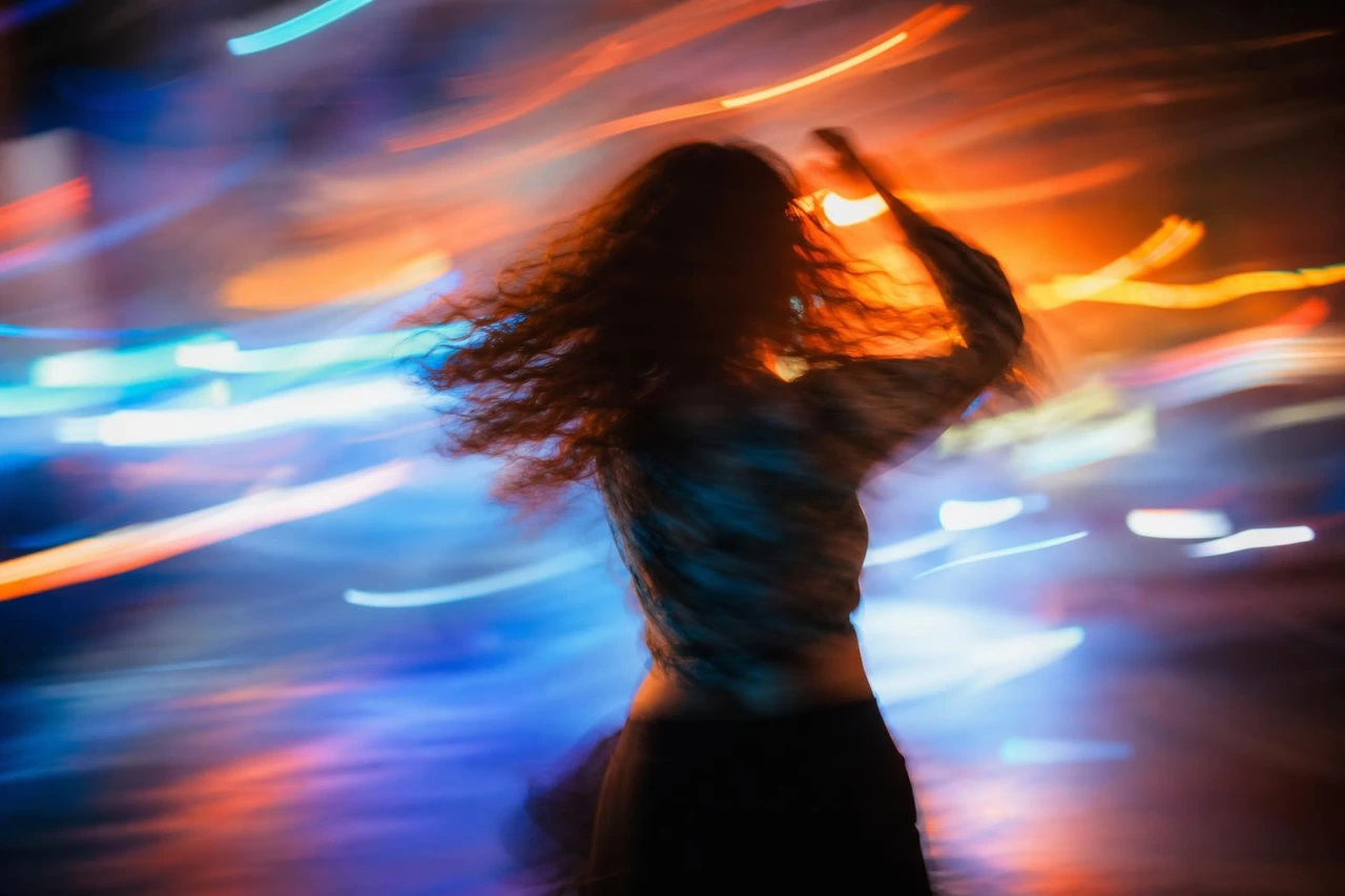 Create a cinematic abstract portrait of a blurred figure surrounded by dynamic neon light streaks, blending warm orange tones with cool blue and purple highlights.